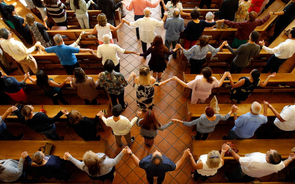 (Vernon Bryant/The Dallas Morning News via AP) Churchgoers hold hands as they sing during a morning service at St. Pius X Church in El Paso, Texas, Sunday, Aug. 4, 2019.