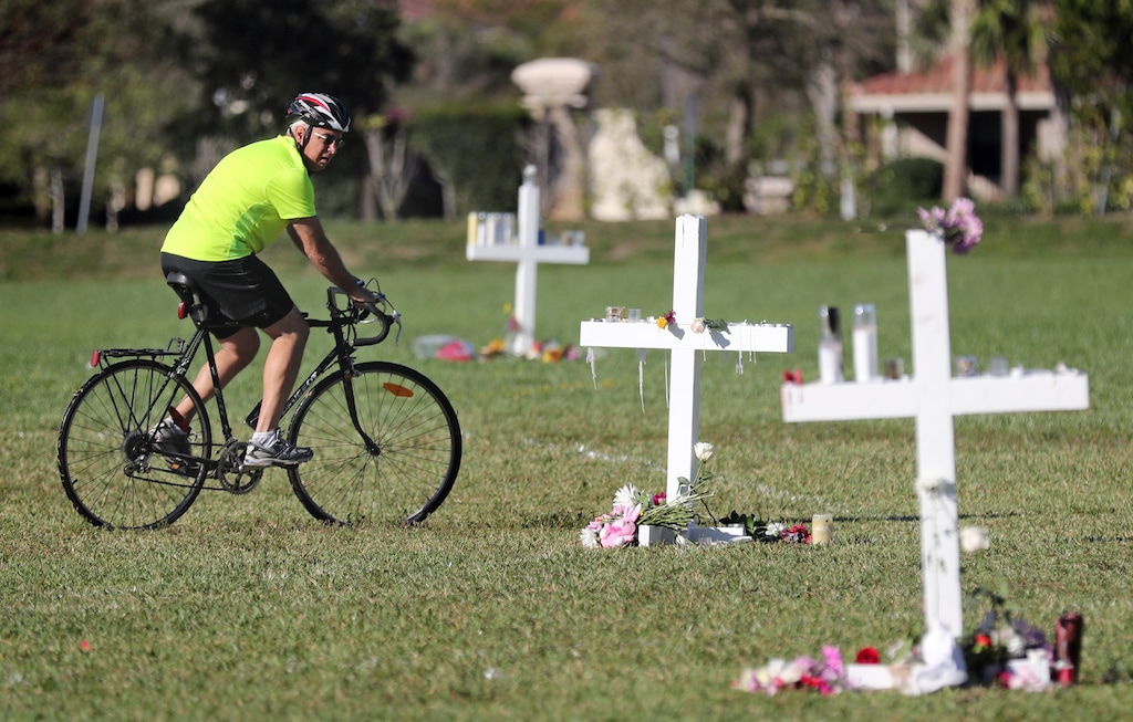 A bicyclist rides between the memorial crosses at Pine Trails Park in Parkland, Fla., Friday, Feb. 16, 2018. The crosses were placed for the victims of the Wednesday shooting at Marjory Stoneman Douglas High School. (Amy Beth Bennett/South Florida Sun-Sentinel via AP)