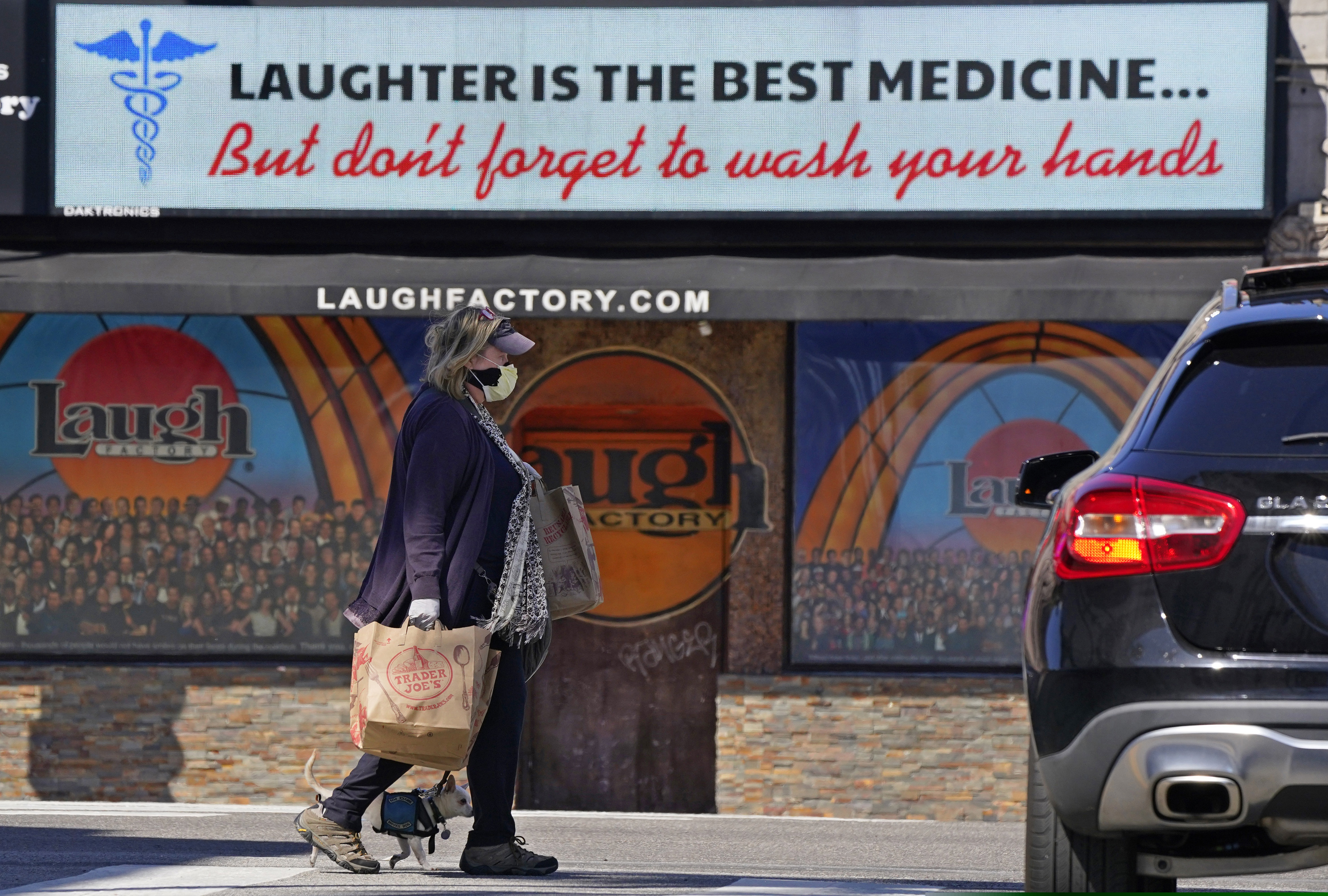 (Mark J. Terrill | AP) In this photo taken Wednesday, March 18, 2020, a woman and her dog walk by the Laugh Factory where a sign urged people to wash their hands in the Hollywood section of Los Angeles. From Disneyland to Yosemite National Park, the Golden State's iconic destinations are closed or shuttering amenities to prevent the spread of the coronavirus pandemic.