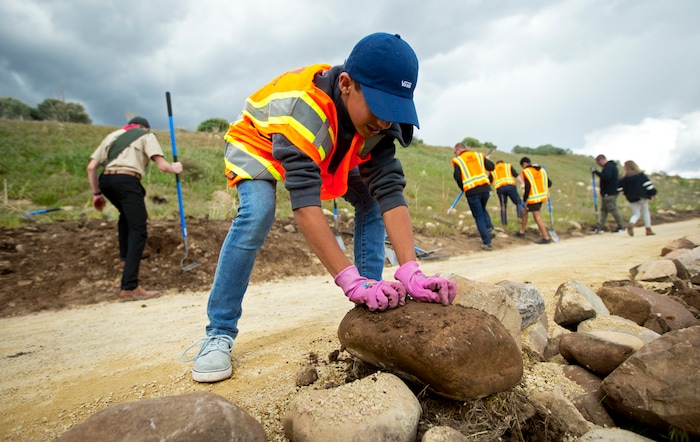 In a Wednesday, May 8, 2019, photo Anthony James, 12, of Lehi, places a rock to keep the path from eroding over time as he and other volunteers help to complete an Eagle Scout Service Project that aims to create a walkable path connecting nearby neighborhoods to Ignite Entrepreneurship Academy and a future park just northwest of the charter school in Lehi, Utah. (Isaac Hale/The Daily Herald via AP)