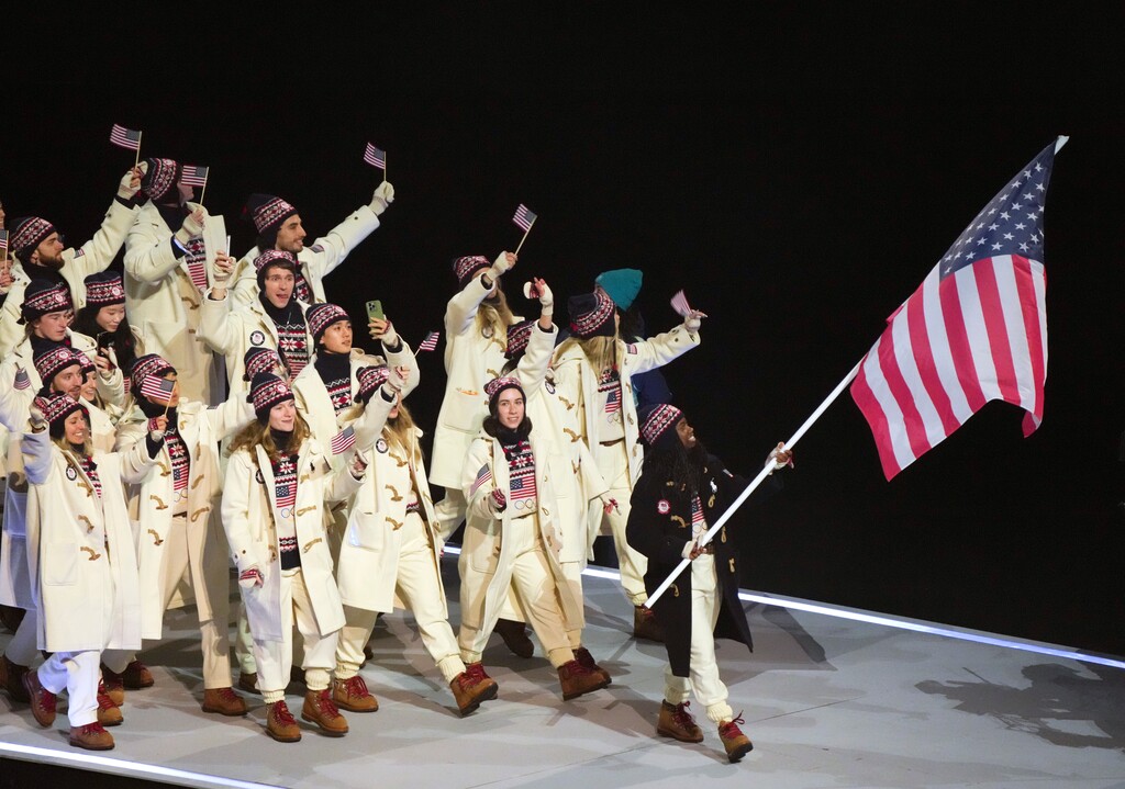 (Gabriela Bhaskar | The New York Times) Erin Jackson carries the American flag as athletes from the United States enter the stadium during the opening ceremony of the 2026 Milan Cortina Winter Olympics at San Siro stadium in Milan, on Friday, Feb. 6, 2026.