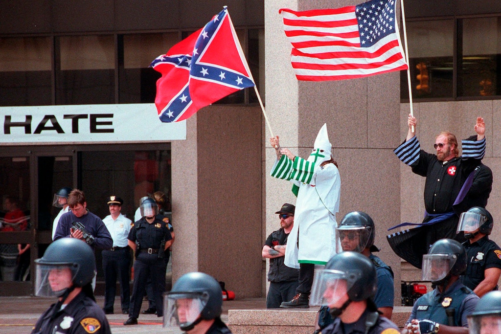 FILE - In this Saturday, Aug. 21, 1999 file photo, Sheldon White, the Grand Dragon of Michigan, hooded at background center, and Jeffrey Berry, background right, the Imperial Wizard of the American Knights of the Ku Klux Klan, wave flags and salute the crowd during the group's rally in downtown Cleveland. The sign at left reads "DON'T HATE." (Jeffrey A. Camarati/The Morning Journal via AP)