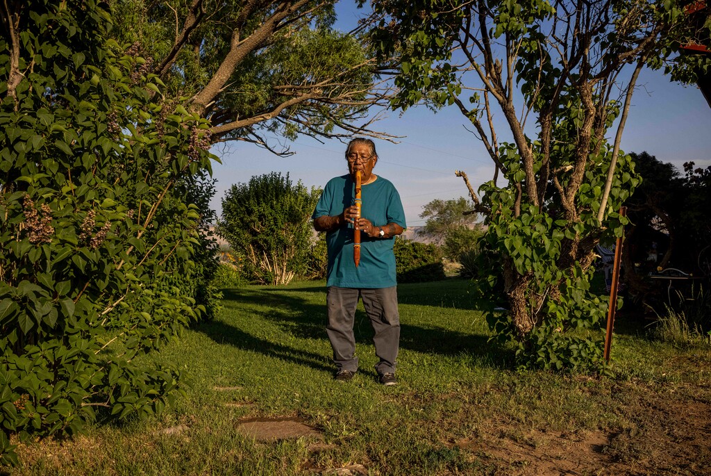 (Sharon Chischilly | The New York Times) Norman Lopez, 78, plays a flute outside of his home in Towaoc, Colo., June 15, 2021. He said a boarding school teacher in Colorado smashed his hand-carved flute and threw it in the trash. Thousands of Native American children attended U.S. boarding schools designed for "civilizing the savage." Many died. Many who lived are reclaiming their identity.