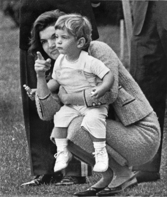 FILE - In this Oct. 15, 1962 file photo, John F. Kennedy, Jr., son of the president, watches from the rose garden with his mother Jacqueline Kennedy as his father gives a formal greeting to Algerian Premier Ahmed Ben Bella during ceremony on the White House grounds in Washington. A documentary film on John Kennedy Jr.'s life opens Friday, July 22, 2016, in select theaters. It also airs on Spike TV at 9 p.m. EDT on Aug. 1, and a DVD release is set for Aug. 16. (AP Photo/William C. Allen)