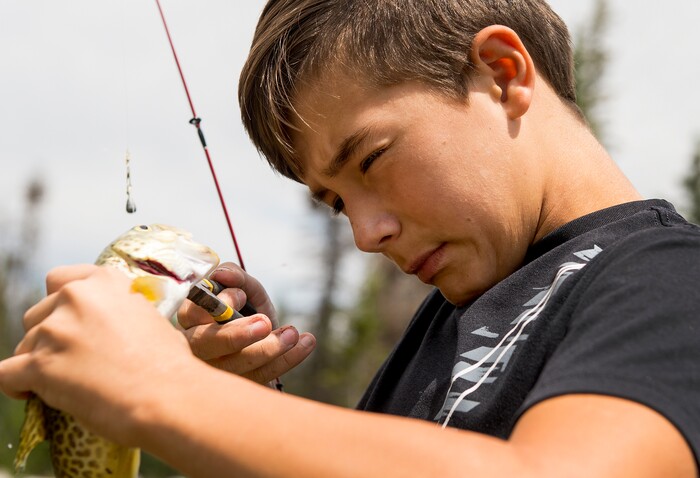 (Leah Hogsten  |  The Salt Lake Tribune)  Tyler Briggs tries to remove a lodged hook deep in the body of a tiger trout while fishing with his father at Mirror Lake, Aug. 6, 2017.