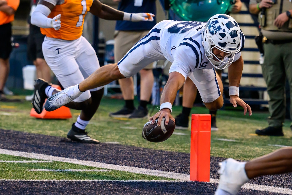 (Tyler Tate | AP) Utah State quarterback Bryson Barnes goes airborne and reaches the football across the goal line for a touchdown during the second half of an NCAA college football game against UTEP, Saturday, Aug. 30, 2025, in Logan, Utah.