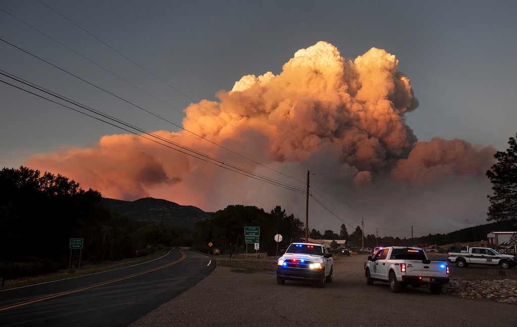 (Morgan Timms/Taosnews.com via AP) In this photo taken Thursday, May 31, 2018, and provided by Taosnews.com, officials confer as smoke rises from the Ute Park Fire in Ute Park, N.M. Evacuation centers have been set up in northeastern New Mexico as heavy smoke from a wildfire has forced residents from Cimarron and the surrounding areas to leave their homes.