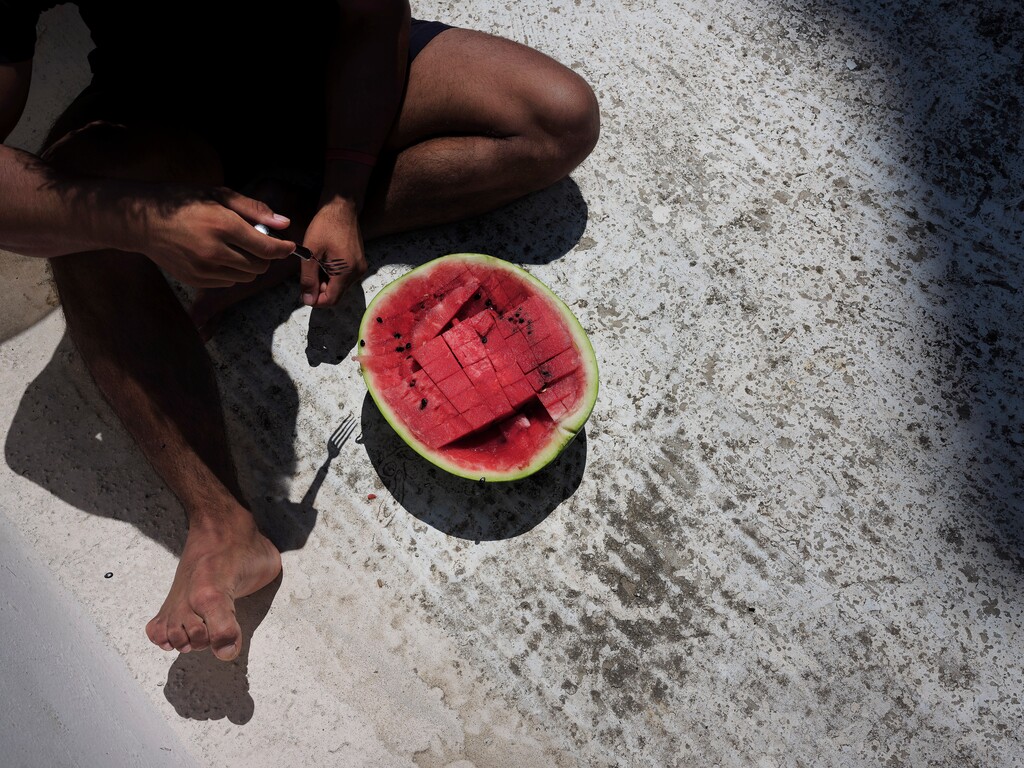 (Myrto Papadopoulos | The New York Times) A homeless refugee from Afghanistan eats watermelon outside the rooftop shack where he lives in Athens, Greece, July 22, 2020.