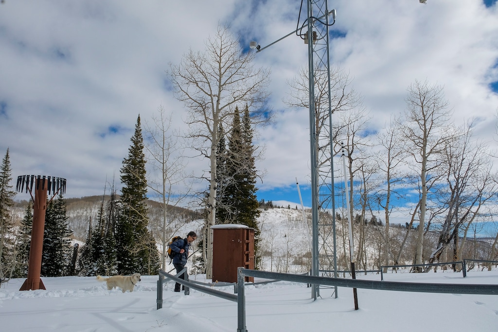 (Leah Hogsten | The Salt Lake Tribune) Jordan Clayton, supervisor with Utah Snow Survey for the Natural Resources Conservation Service (NRCS) shown with his dog Gus, at the Daniels Strawberry Snotel or snow telemetry network site, Feb. 3, 2021. The tall tower is equipped with wind, temperature, snow depth and solar radiation sensors. The brown tower, left, is a precipitation gage. All the sensors send information to the equipment shelter, right, where the data is uploaded to the NRCS. Snotels are located in often remote, high-elevation mountain watersheds and monitor snowpack, precipitation, soil moisture, temperature, and other climatic conditions affecting Utah's watersheds. Since roughly 95% of Utah's water supply comes from snowmelt, Snow Survey staff use Snotel data to forecast summer water supply conditions in the state's watersheds.