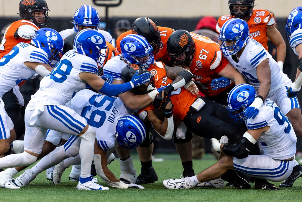 BYU defensive end Logan Lutui, left, defensive tackle Bruce Mitchell, center, and defensive end Tyler Batty, right, tackle Oklahoma State running back Ollie Gordon II (0) in the first half of an NCAA college football game Saturday, Nov. 25, 2023, in Stillwater, Okla. (AP Photo/Mitch Alcala)