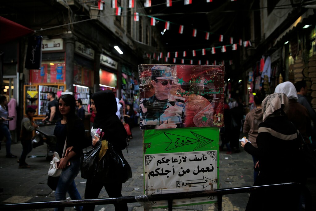 (Hassan Ammar | The Associated Press) Syrians walk past a picture showing Syrian President Bashar Assad with Arabic that reads, "We apologize for your inconvenience, We are working for you. Exit," as shop at the Hamadiyah market in the Old City of Damascus, Syria, Thursday, April 12, 2018. The streets of Damascus were packed with people Thursday evening either going out to shop in one of the city's main markets to hanging out with families and friends at the capital's cafes, restaurants and sweets shops, people mostly appeared not concerned about a possible U.S. strike on the country going on with their lives as usual.