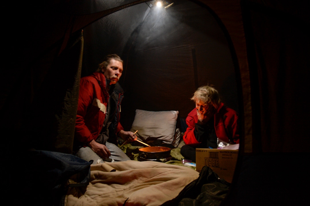 (Leah Hogsten  |  The Salt Lake Tribune)  Ron Barrett, 55, and his wife Katherine Barrett, 54, who are homeless, try to stay warm in their tent from the meager heat from a ceramic pot filled with candle wax. Their cold hands are blacken by the soot rising from the burning candle on a night that temperatures dropped to 12 degrees in Salt Lake City. "It's crazy, you gotta be able to have a sense of humor," said Ron Barrett, 55, of the life circumstances that resulted in life on the streets for he and Katherine since 2017. The Barretts are trying to find housing through a Shelter Plus Care housing voucher through the Salt Lake City Housing Authority. The couple says they refuse to stay in the state's largest homeless shelter, The Road Home on Rio Grande Street, because of past threats of violence from other residents.