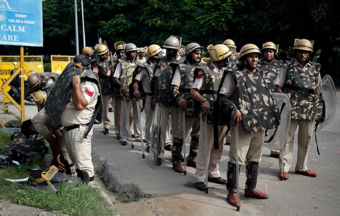 An Indian policeman puts on a bullet proof vest as he joins others on a road leading to a court in Panchkula, India, Friday, Aug. 25, 2017.  Several north Indian cities were under a security lock down Friday as a court was expected to issue a verdict in a rape case involving a man who calls himself Saint Dr. Gurmeet Ram Rahim Singh Ji Insan, the flamboyant leader of a quasi-religious sect. (AP Photo/Altaf Qadri)
