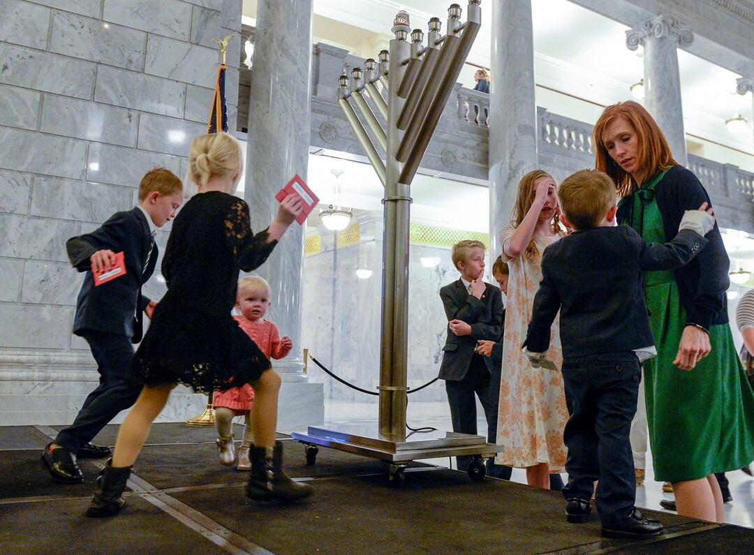 Leah Hogsten  |  The Salt Lake Tribune   Jennie Taylor tends to one of her sons as her children dance under the Menorah during the 12th annual Hanukkah celebration at the Utah Capitol, Dec. 2, 2018. The event was also dedicated as 'A Salute to a Hero', in tribute to her late husband, Maj. Brent Taylor of North Ogden.