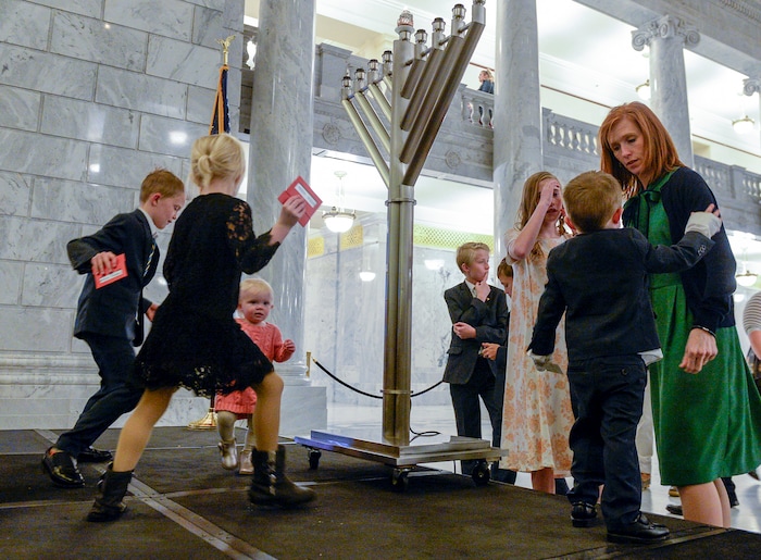 Leah Hogsten  |  The Salt Lake Tribune   Jennie Taylor tends to one of her sons as her children dance under the Menorah during the 12th annual Hanukkah celebration at the Utah Capitol, Dec. 2, 2018. The event was also dedicated as 'A Salute to a Hero', in tribute to her late husband, Maj. Brent Taylor of North Ogden.