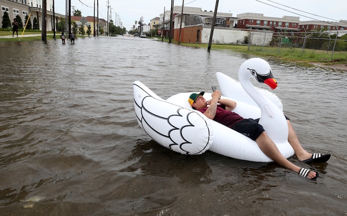 (Jennifer Reynolds | The Galveston County Daily News via AP) Julio Ostio sits in an inflatable swan as he floats down 16th Street near Strand Street in Galveston, Texas, on Saturday, Aug. 26, 2017, as he texts friends during a break in the rain from Hurricane Harvey.