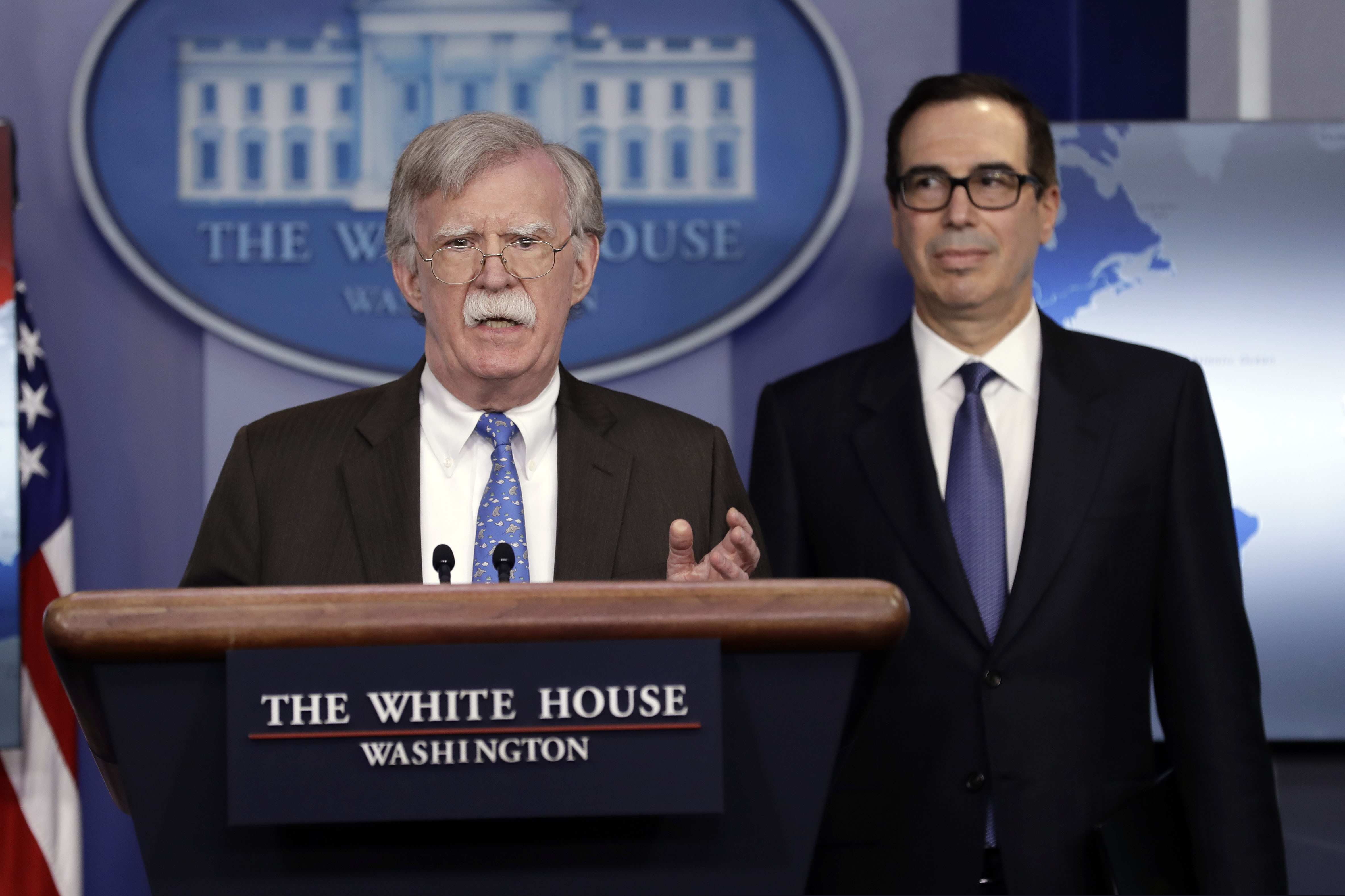 (Evan Vucci | The Associated Press) National security adviser John Bolton speaks as Treasury Secretary Steven Mnuchin listens during a press briefing at the White House on Jan. 28, 2019, in Washington. The Trump administration imposed sanctions this week on the state-owned oil company of Venezuela in a move to pressure President Nicolas Maduro to cede power to U.S.-backed opposition.