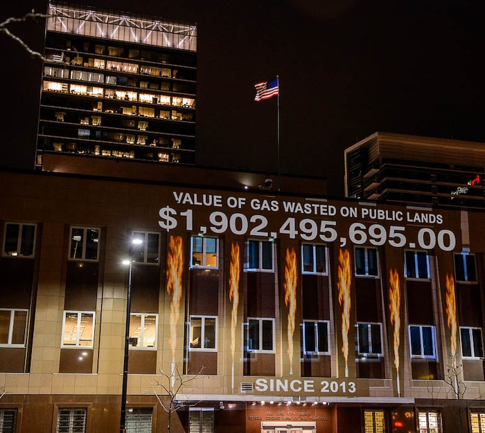 (Trent Nelson | The Salt Lake Tribune)
In a visual protest, Alliance for Better Utah projects the total dollar value of natural gas lost on public lands since 2013 due to venting, flaring, and leaking onto the side of Federal Reserve Building in Salt Lake City, Thursday April 5, 2018.