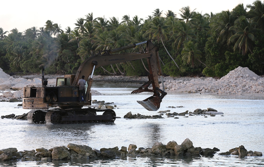 (Rob Griffith | AP file photo) An excavator moves rocks and sand in 2015 to aid in the construction of sea walls around the airport on Majuro Atoll in the Marshall Islands. Climate change poses an existential threat to places like the Marshall Islands, which protrude only 6 feet (2 meters) above sea level in most places. King tides, when the alignment of the Earth, moon and sun combine to produce the most extreme tidal effects, and storm surges cause floods that contaminate fresh water, kill crops, and erode land. As a result, some Marshallese think an exodus as inevitable, while others are planning to stay and fight.