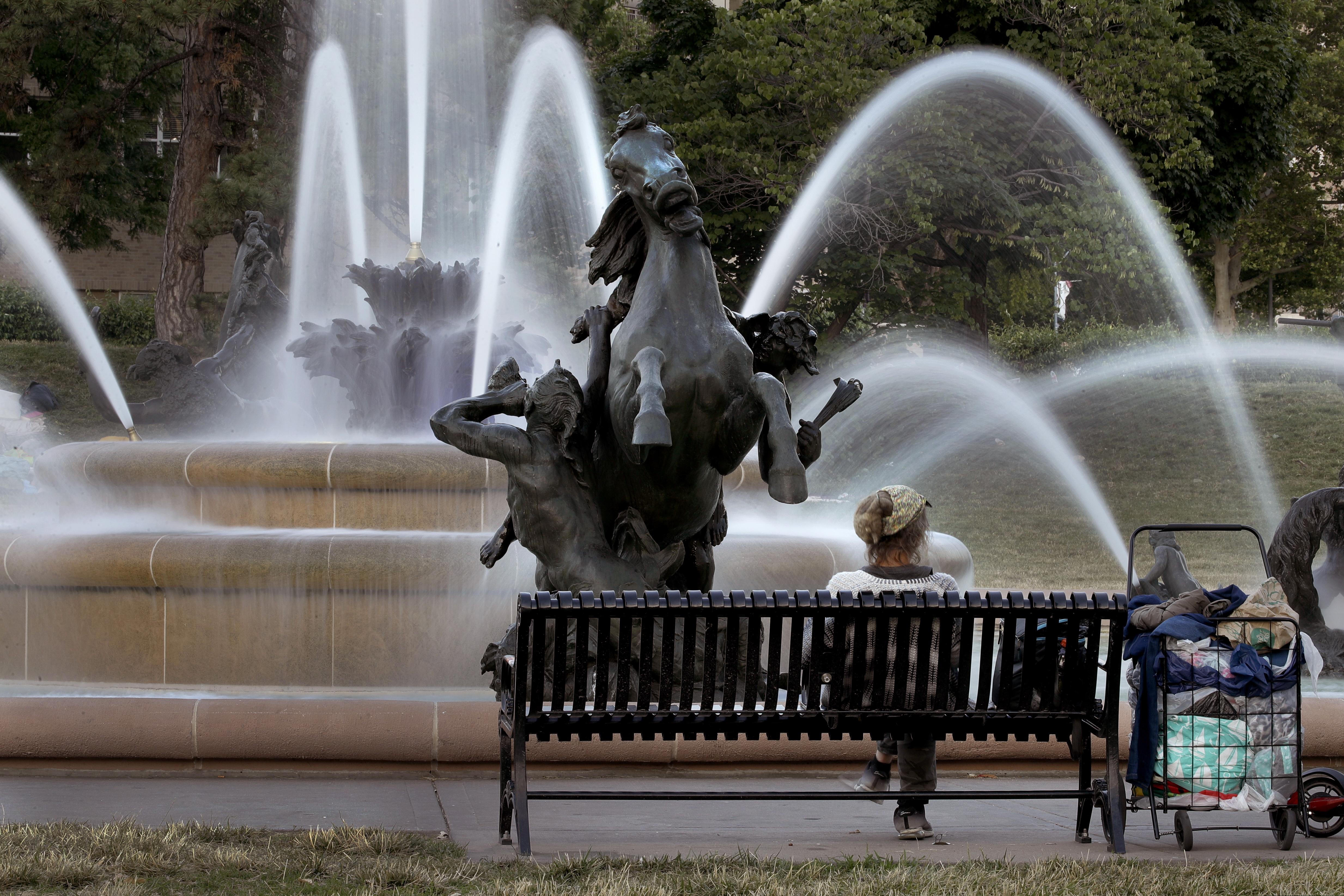(AP Photo | Charlie Riedel)
In this photo taken Tuesday, June 23, 2020, a homeless woman sits on a bench near the J.C. Nichols fountain in Kansas City, Mo. The city's board of parks and recreation is considering a proposal to remove the J.C. Nichols name from the fountain and a nearby street as it addresses racial concerns about the influential local developer. Nichols developed some of the area's most desirable neighborhoods as well as the city's Country Club Plaza shopping district in the early 1900s, but excluded Blacks, Jews and other minorities using deed restrictions on his properties.