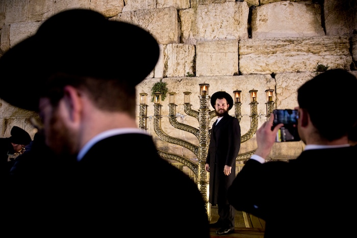 An ultra Orthodox Jewish man poses for a picture near a large Hanukiah, a Jewish candle holder traditionally used during the Hanukkah holiday, on the third eve of Hanukkah at the Western Wall, the holiest site where Jews can pray in Jerusalem's old city, Thursday, Dec. 14, 2017. (AP Photo/Sebastian Scheiner)