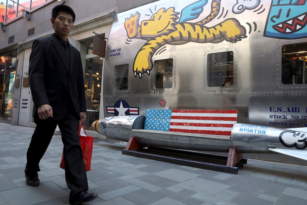 A man walks past a U.S. fashion apparel store with a bench shaped like a bomb with a U.S. flag in Beijing Monday, May 6, 2019. U.S. President Donald Trump raised pressure on China on Sunday, threatening to hike tariffs on $200 billion worth of Chinese goods in a tweet that sent financial markets swooning. Trump's comments, delivered on Twitter, came as a Chinese delegation was scheduled to resume talks in Washington on Wednesday aimed at resolving a trade war that has shaken investors and cast gloom over the world economy. (AP Photo/Ng Han Guan)