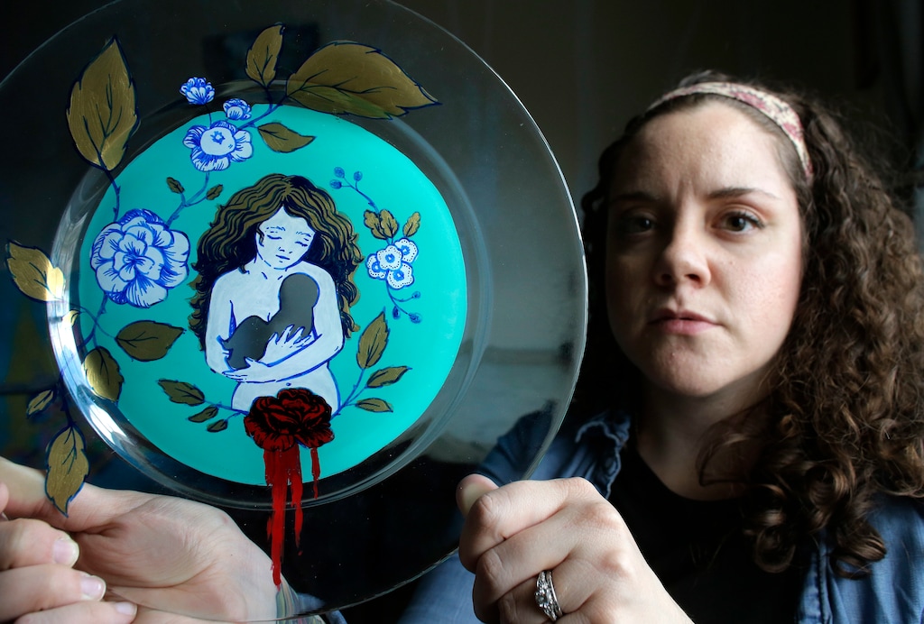 In this Thursday, April 26, 2018, photo, artist Ashley MacLure holds her painting "The Dream" created from acrylic paint and color marker on a glass plate, at her home in Milford, Mass. The blank space at the center is meant to represent the absence of a child due to a miscarriage. MacLure hopes her paintings, inspired by miscarriage, will help end the stigma of pregnancy loss. (AP Photo/Steven Senne)