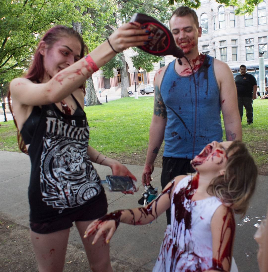  (Rick Egan  |  The Salt Lake Tribune)       Breanna Davis pours hershey syrup with red food coloring onto Gaia Bailey, as Eli Bailey watches during the 11th annual Salt Lake Zombie Walk, Sunday, Aug. 26, 2018.