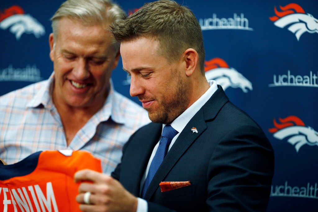 Case Keenum, front, admires his new jersey as John Elway, general manager of the Denver Broncos, looks on during a news conference to introduce him as the new starting quarterback of the Broncos at the NFL football team's headquarters Friday, March 16, 2018, in Englewood, Colo. (AP Photo/David Zalubowski)