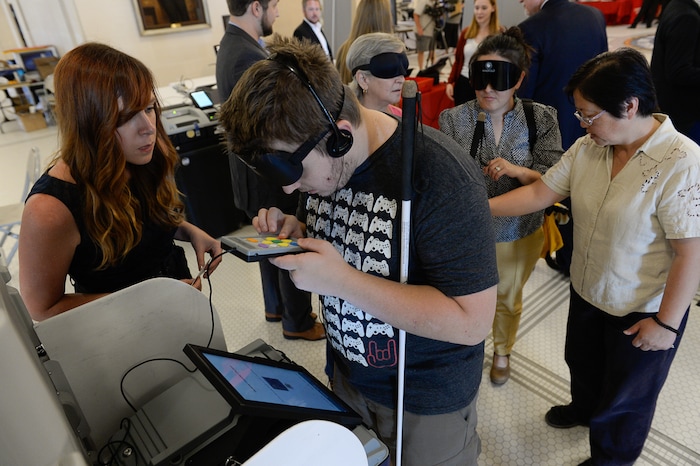 (Francisco Kjolseth  |  The Salt Lake Tribune)  Sean Schilling who is visually impaired, is guided through the use of a voting machine manufactured by Voting Solutions by Bliss Foutty, President of Election IQ. Companies demonstrated new voting machines that the state is considering buying during a hands on presentation at the Capitol on Wednesday, Aug. 2, 2017.