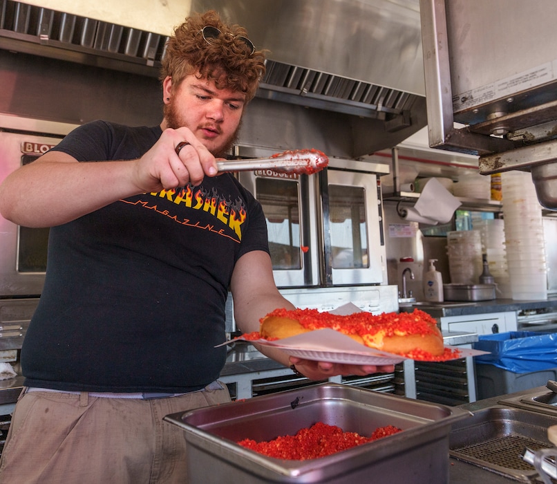(Leah Hogsten | The Salt Lake Tribune) Kolby Servoss sprinkles hot cheetos on a pretzel with nacho cheese at the Soft & Hot Pretzels stand, at the Utah State Fair, Sept. 9, 2022. 