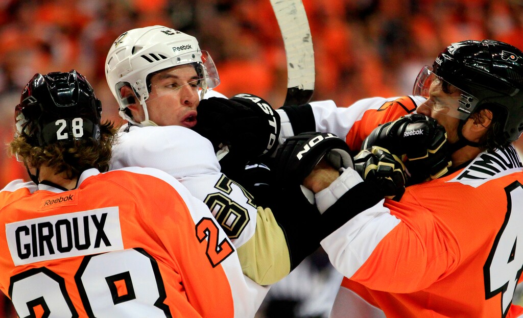 FILE - In this April 15, 2012, file photo, Philadelphia Flyers Claude Giroux, left, holds on to Pittsburgh Penguins' Sidney Crosby as Kimmo Timonen, right, lands a punch to Crosby's jaw during the first period of Game 3 in a first-round NHL Stanley Cup playoffs hockey series in Philadelphia. The NHL’s divisional playoff format was brought back specifically to ignite old and create new rivalries, which has been a successful venture even if hate looks different than it did in the days of the “Broad Street Bullies.” Playoff rivalries are no longer about dropping the gloves or even laying out bone-crushing hits like in past eras. (AP Photo/Tom Mihalek, File)