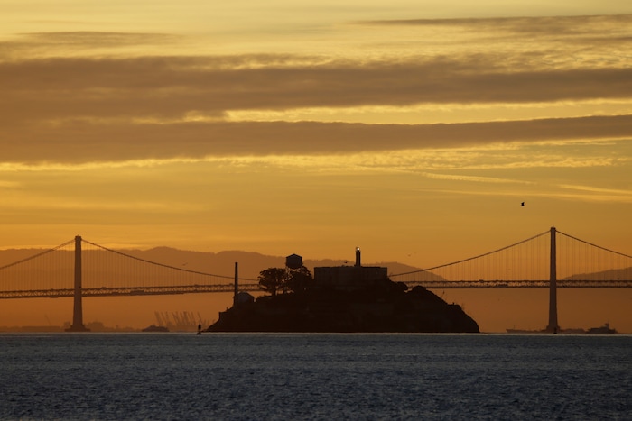 (Eric Risberg | AP) In this photo taken Feb. 1, 2018, Alcatraz Island is seen at sunrise on San Francisco Bay in this view from Sausalito, Calif. In the background is the San Francisco-Oakland Bay Bridge. The week of Nov. 18, 2019, marks 50 years since the beginning of a months-long Native American occupation at Alcatraz Island in the San Francisco Bay. The demonstration by dozens of tribal members had lasting effects for tribes, raising awareness of life on and off reservations, galvanizing activists and spurring a shift in federal policy toward self-determination.