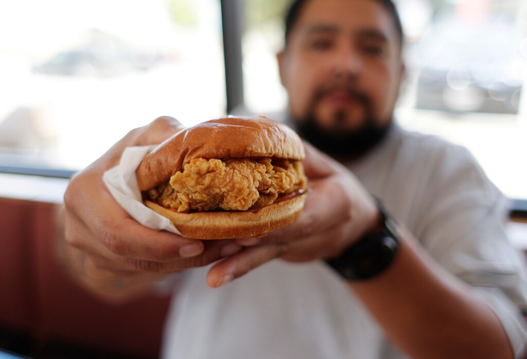 (Eric Gay | AP file photo) Randy Estrada eats a chicken sandwich at a Popeyes in Kyle, Texas. After Popeyes added a crispy chicken sandwich to their fast-fast menu, the hierarchy of chicken sandwiches in America was rattled, and the supremacy of Chick-fil-A and others was threatened. It’s been a trending topic on social media, fans have weighed in with YouTube analyses and memes, and some have reported long lines just to get a taste of the new sandwich.