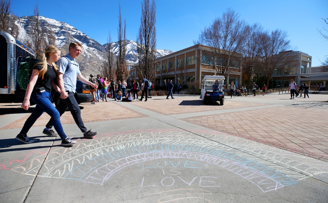(George Frey  |  special to The Salt Lake Tribune) Two BYU students hold hands as they walk past other BYU students in front of the Ernest L. Wilkinson Student Center on the campus of Brigham Young University to protest BYUÕs rollback of a newly announced policy change on LGBTQ students on March 5, 2020 in Provo, Utah.