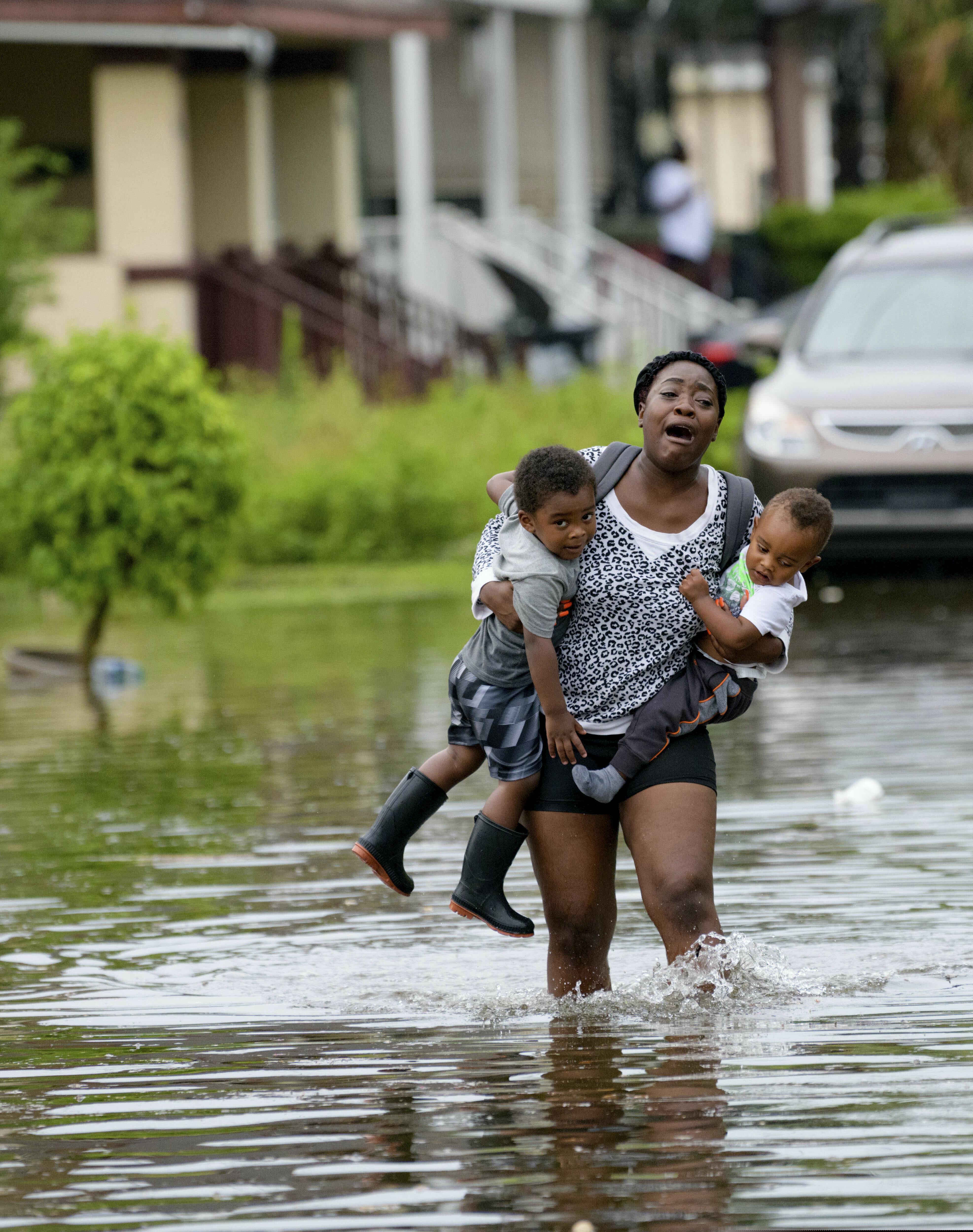 (Matthew Hinton | AP Photo) Terrian Jones reacts as she feels something moving in the water at her feet as she carries Drew and Chance Furlough to their mother on Belfast Street near Eagle Street in New Orleans after flooding from a storm dumped lots of rain on Wednesday, July 10, 2019.