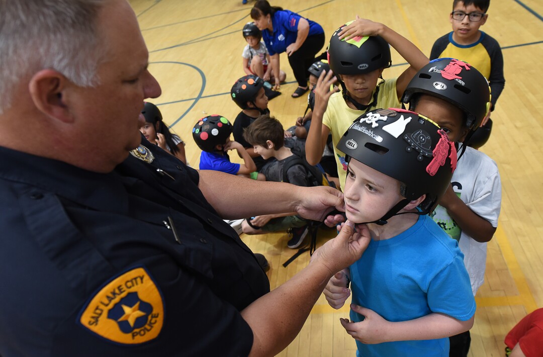 (Francisco Kjolseth  |  The Salt Lake Tribune)  Detective Greg Wilking helps kids set up their new helmets. In advance to the upcoming Tour of Utah bicycle race, more than 50 Salt Lake City-area kids received a new bicycle helmet at the Capitol West Boys & Girls Club on Tuesday, July 31, 2018. As part of UnitedHealthcare's Pro Cycling team and community outreach program to keep kids healthy and active, team cyclists Jonny Clarke and Sebastian Haedo engage the kids in a few warm up routines before getting on the bike.