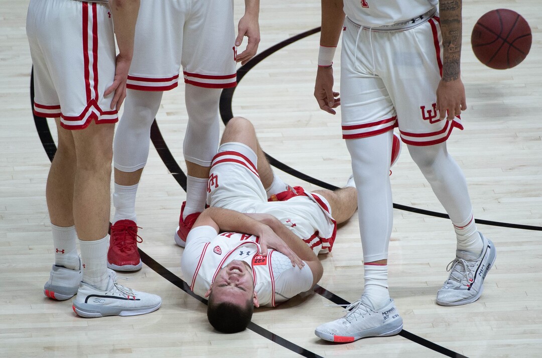 (Francisco Kjolseth  | The Salt Lake Tribune) Utah Utes guard Rylan Jones (15) lies on the floor in pain after colliding with USC Trojans forward Chevez Goodwin (1) in PAC-12 basketball action at the Jon M. Huntsman Center, on Saturday, Feb. 27, 2021.