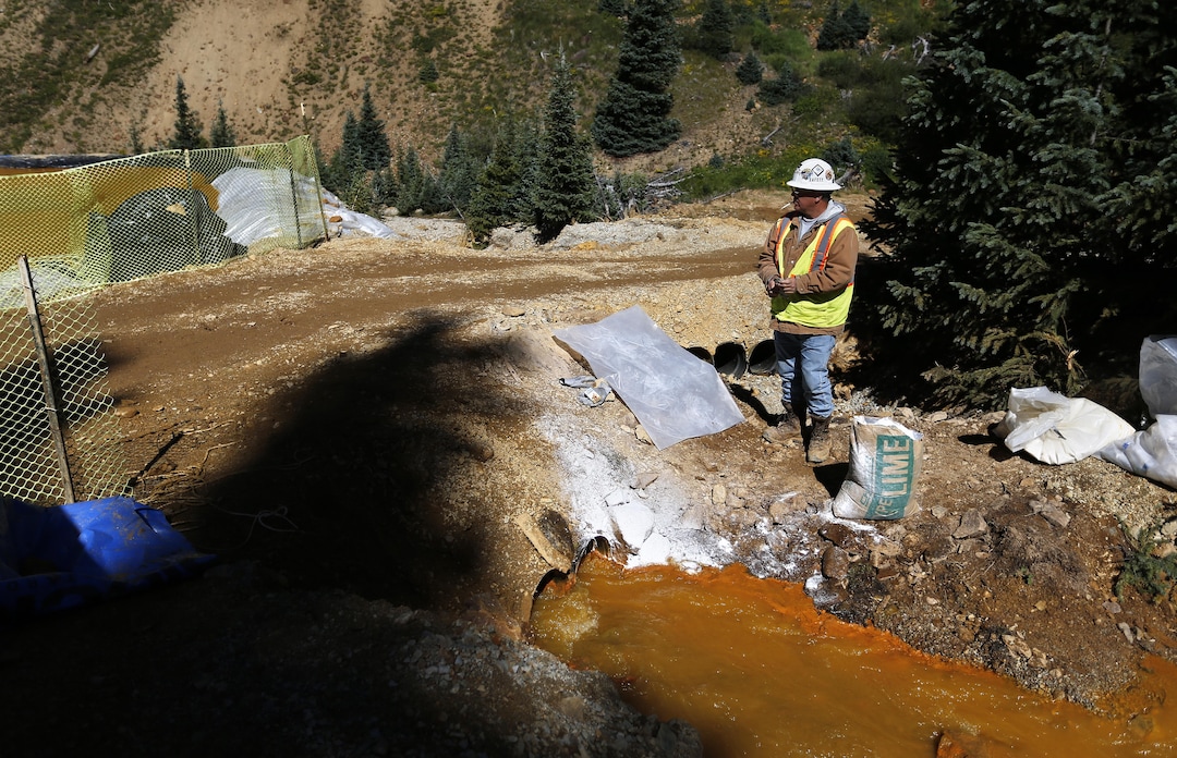 FILE - In this Aug. 14, 2015 file photo, an Environmental Protection Agency contractor keeps a bag of lime on hand to correct the PH of mine wastewater flowing into a series of sediment retention ponds, part of danger mitigation in the aftermath of the blowout at the site of the Gold King Mine, outside Silverton, Colo. Federal officials say they have suspended cleanup work and investigations covering 10 mining sites in four states to guard against a repeat of last months massive wastewater spill from an inactive Colorado gold mine. Details provided to The Associated Press show the order applies to three sites in California, four in Colorado, two in Montana and one in Missouri. (AP Photo/Brennan Linsley, file)