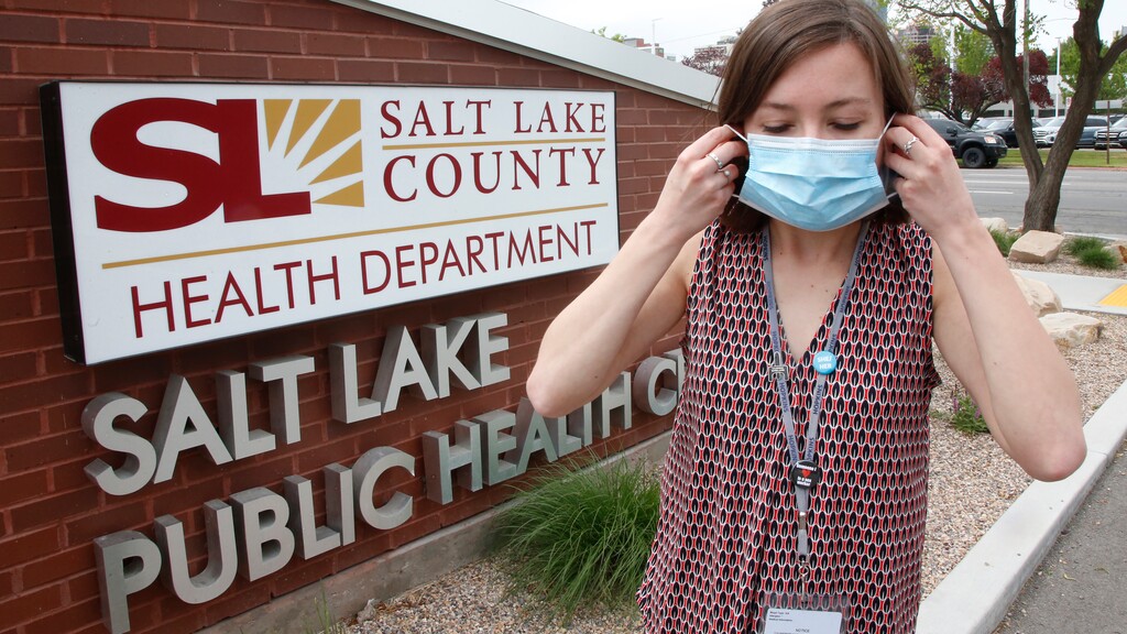 In this Tuesday, May 19, 2020, photo, health investigator Mackenzie Bray adjusts her mask at the Salt Lake County Health Department, in Salt Lake City. Bray normally works to track contacts for people with sexually transmitted diseases, but she was re-assigned during the coronavirus pandemic. She is now one of 130 people at this county health department assigned to track down COVID-19 cases in Utah's urban center around Salt Lake City. The investigators, many of them nurses, each juggle 30 to 40 cases that can include a total of several hundred people. (AP Photo/Rick Bowmer)
