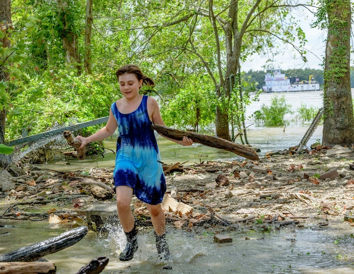 (Matthew Hinton | AP Photo) A towing vessel moves along the Mississippi River, top right, as Tallulah Campbell, 8, clears out driftwood and other debris in preparation of Tropical Storm Barry near New Orleans, La., Thursday, July 11, 2019. The area is normally a driveway at her family's home that is one of the few on land called batture on the outside of the Mississippi River levee at the border of Orleans and Jefferson Parishes. All boat traffic has been ordered to stop by Friday morning in preparation for the storm.