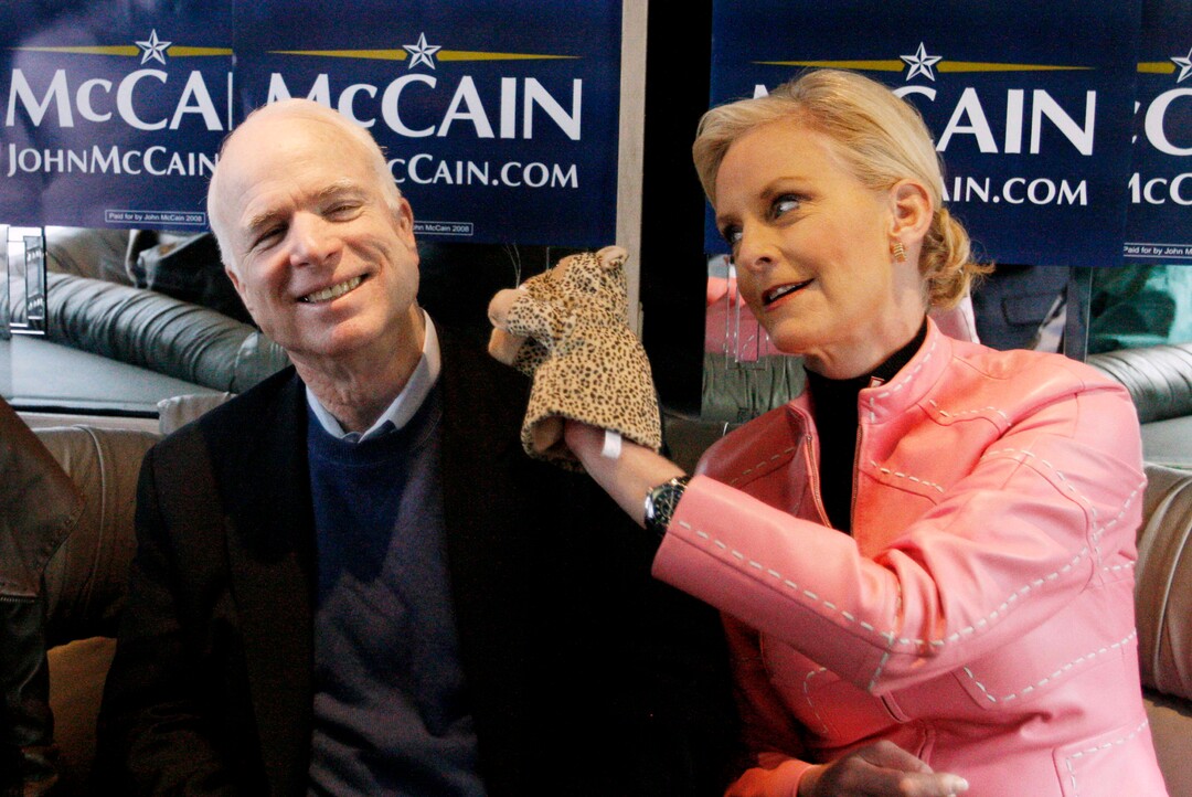 FILE - In this Jan. 19, 2008, file photo, Cindy McCain, wife of Republican presidential hopeful Sen. John McCain, R-Ariz., uses a cheetah hand puppet to make her husband laugh as they ride the "Straight Talk Express" campaign bus to a polling station in Charleston, S.C., on the day of South Carolina's Republican presidential primary. Arizona Sen. McCain, the war hero who became the GOP's standard-bearer in the 2008 election, has died. He was 81. His office says McCain died Saturday, Aug. 25, 2018. He had battled brain cancer. (AP Photo/Charles Dharapak, File)