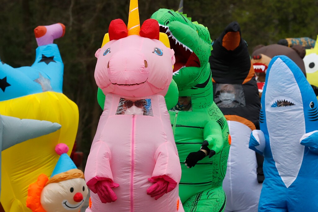 In this Monday, May 11, 2020 photo, members of the T-Rex Walking Club walk through a neighborhood in Ferndale, Mich. The group takes its unannounced strolls through neighborhoods on a quest to bring smiles to the faces of kids, and a few adults, while under Michigan's stay-at-home order due to the COVID-19 pandemic. (AP Photo/Carlos Osorio)
