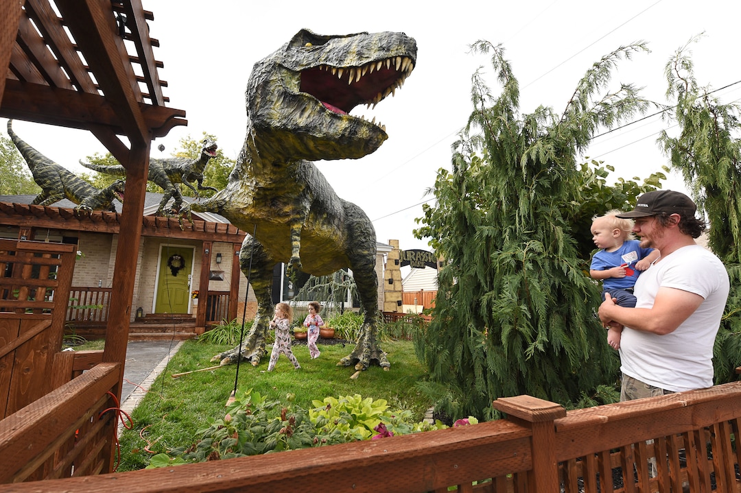 (Francisco Kjolseth  |  The Salt Lake Tribune)  Ammon Smith holds his nephew Lincoln Smith, 1, as his daughter Lola, 3, and her cousin Penny Smith, 3, run around below a giant T-Rex Ammon built for Halloween in his front yard at 1542 S. 900 East in Salt Lake City. The giant dinosaur, along with a pair of velociraptors and pterodactyls, was made from mostly recycled products. The part-time stay-at-home dad, who made a giant King Kong last year, started construction back in August as he assembled recycled wood, chicken wire, foam, aluminum foil and spray paint for the 12-by-32-foot Jurassic centerpiece and companion pieces.