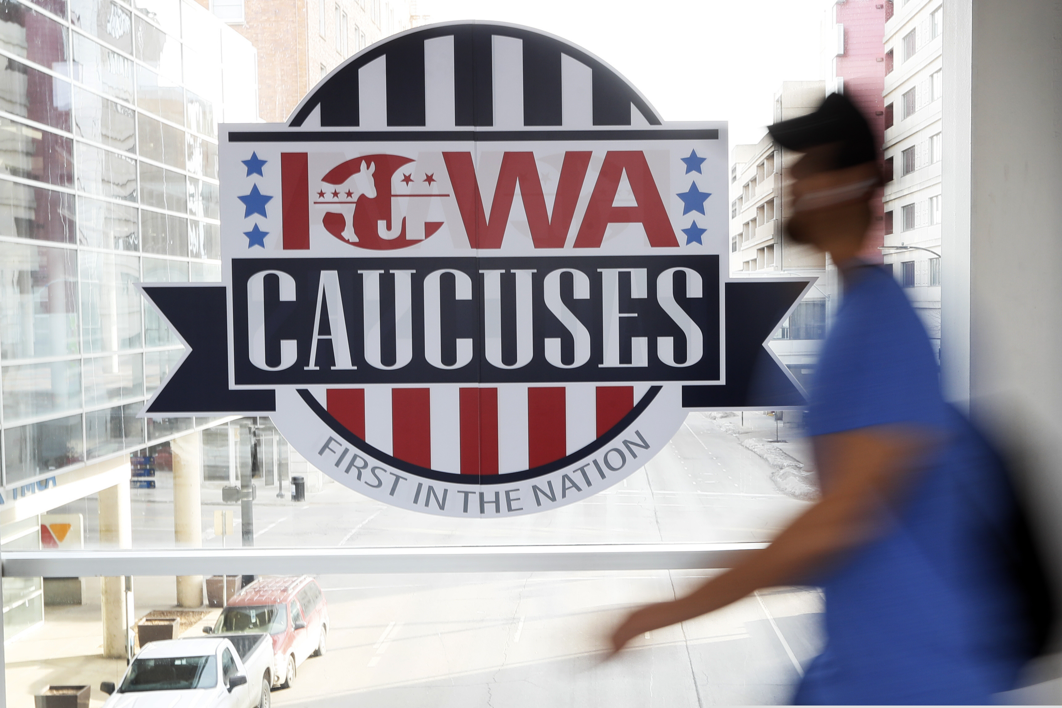 (Charlie Neibergall | AP) A pedestrian walks past a sign for the Iowa Caucuses on a downtown skywalk, Tuesday, Feb. 4, 2020, in Des Moines, Iowa.