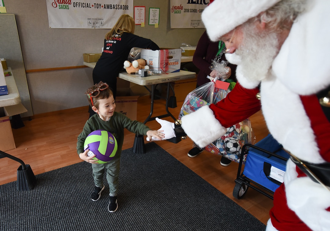 (Francisco Kjolseth  |  The Salt Lake Tribune)  Oliver Sanderson, 3, is greeted by Santa played by Merlin Taylor as they stop in to the Granite Education Foundation Santa Sacks workshop in South Salt Lake on Tuesday, Dec. 3, 2019. Sanderson's aunt is one of the social workers who helps identify those families in need as they filled a couple vehicles with sacks bound schools in the district.