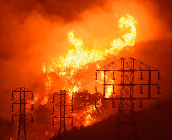 (Mike Eliason | Santa Barbara County Fire Department via AP) In this Saturday, Dec. 16, 2017, photo provided by the Santa Barbara County Fire Department, flames burn near power lines in Sycamore Canyon near West Mountain Drive in Montecito, Calif. One of the largest wildfires in California history is now 40 percent contained but flames still threaten coastal communities as dry, gusty winds are predicted to continue. Some 8,000 firefighters are deployed to the so-called Thomas Fire, which has burned for nearly two weeks and still threatens 18,000 homes. Swaths of Santa Barbara County remain under evacuation orders.