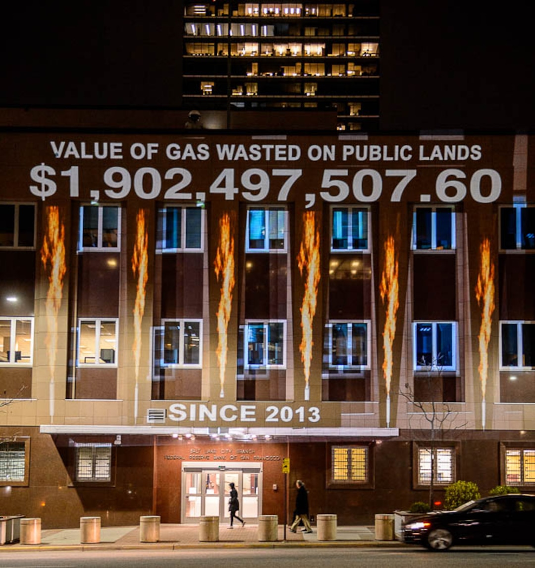(Trent Nelson | The Salt Lake Tribune)  In a visual protest, Alliance for Better Utah projects the total dollar value of natural gas lost on public lands since 2013 due to venting, flaring, and leaking onto the side of Federal Reserve Building in Salt Lake City, Thursday April 5, 2018.