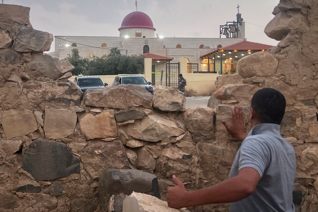 (AP) A man looks through a gap in a stone wall toward a Greek Orthodox church where gunmen opened fire during a funeral hours earlier in Jordan's Hamoud village on Friday, Oct. 23, 2026.