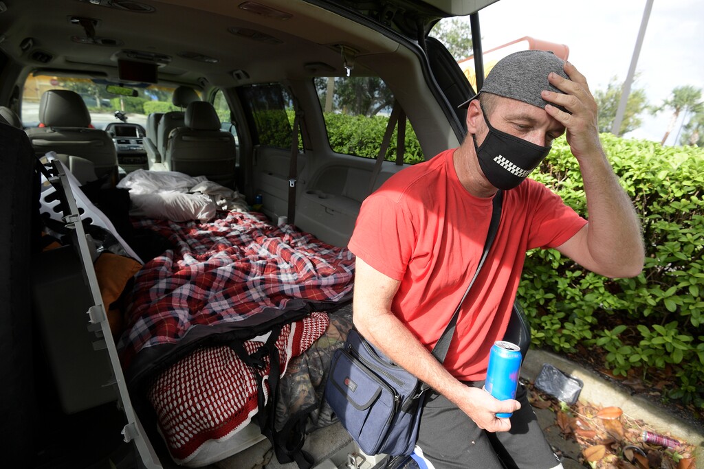 Jeff Lello adjusts his hat while sitting on the back of the van out of which he has been living, in the parking lot of a Cracker Barrel restaurant, since being laid off due to the coronavirus pandemic, Friday, Aug. 21, 2020, in Orlando, Fla. Lello is one of an estimated 20 million Americans living paycheck to paycheck, spending more than 30% of their income on rent, who are likely to experience homelessness at some point, according to the National Coalition for the Homeless. (AP Photo/Phelan M. Ebenhack)